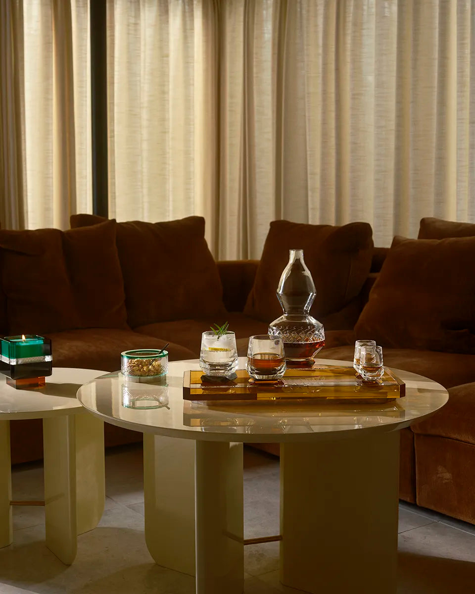 The Majesty Flacon sits on a round table in a moody living room setting, accompanied by whisky glasses and a golden tray, exuding elegance.